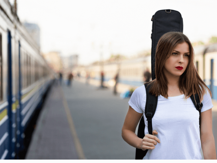 Woman with guitar in case, over her shoulder, at the railway station.