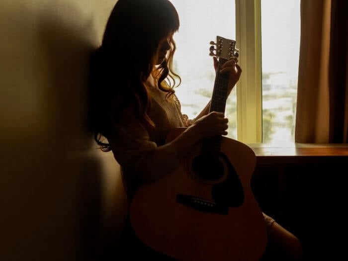 Silhouette of a young woman playing guitar alone in the dark.