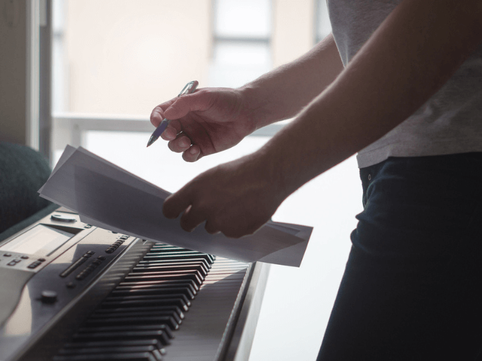 A closeup of someone writing sheet music next to a keyboard.