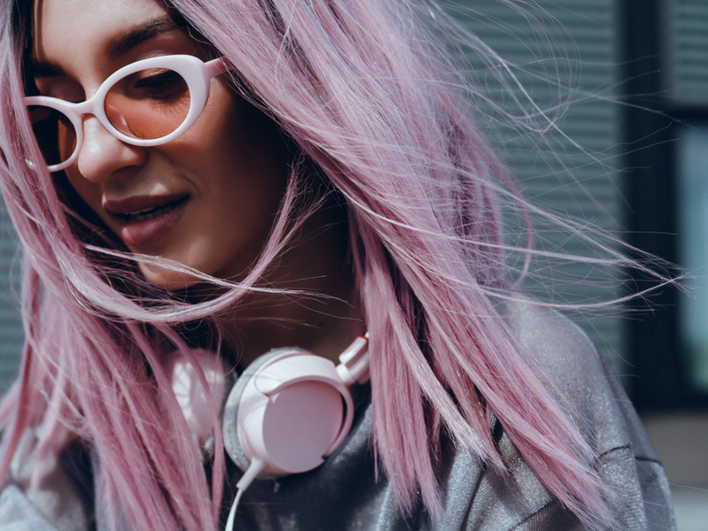 woman with pink hair with headphones and yellow sunglasses on