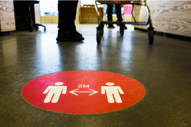 Red round sign printed on ground at supermarket informing people to keep 2 meter distance from each other to prevent spreading Coronavirus
