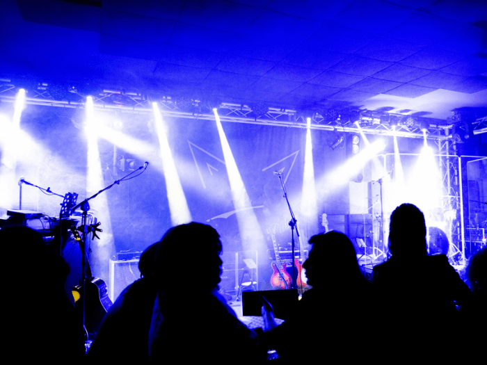 Silhouettes of crowd in front of a small festival stage in blue light.