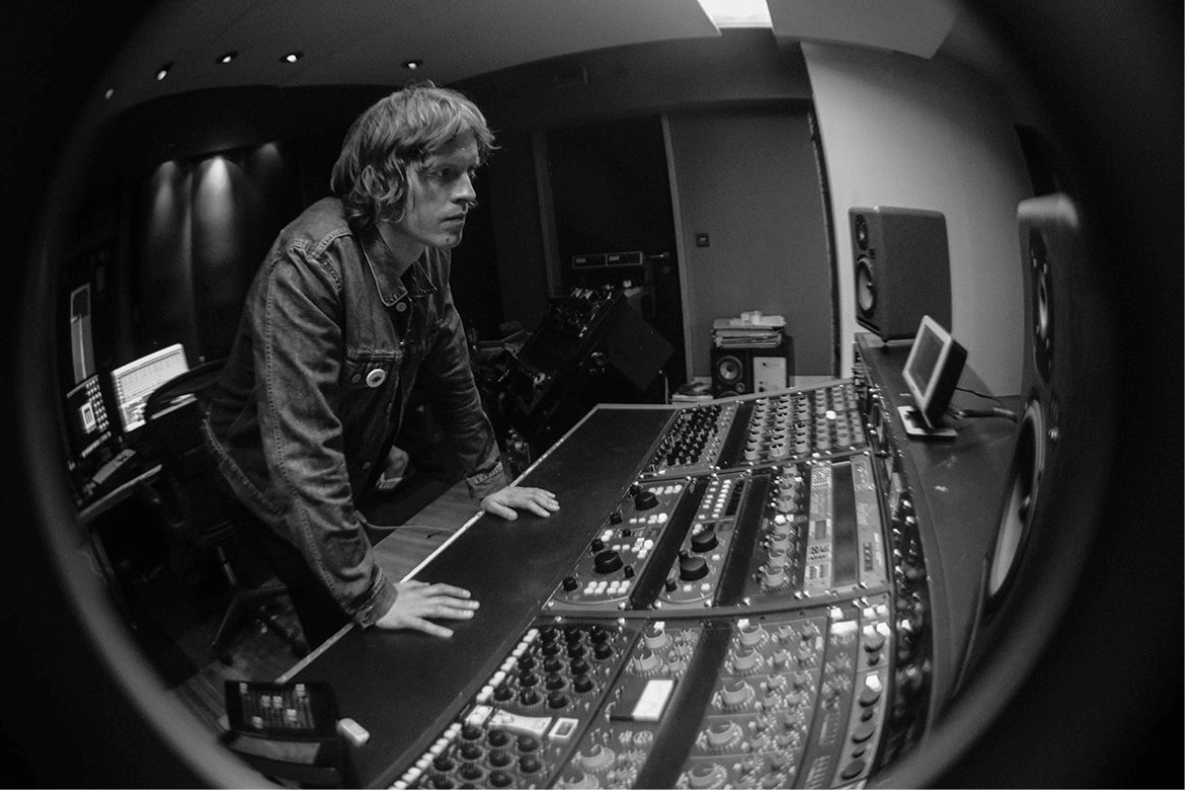 Black and white portrait of Alex Lipinski over a mixing desk in recording studio.