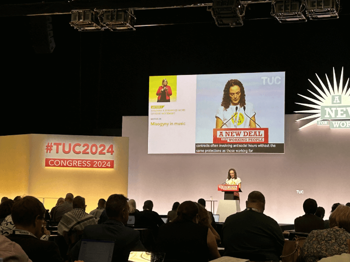 A conference room full of people with a speaker on the stage.