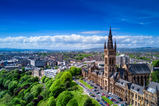 Photograph of an aerial view of Glasgow, the sky above is blue and the trees are bright green.