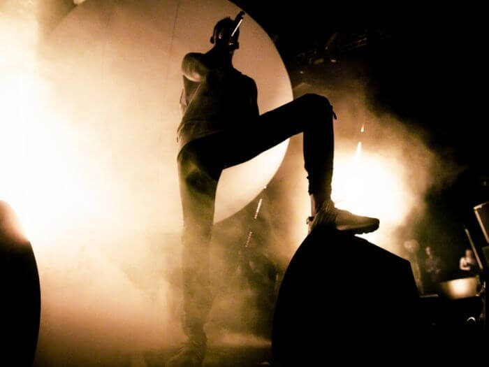 Silhouette of a rap artist on stage. He performs to the crowd against smoke and bright lights.