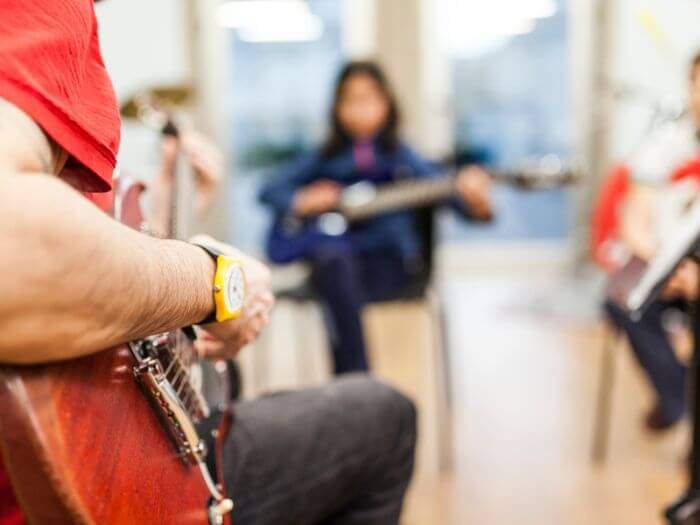 Out of focus shot of a man teaching a group how to play guitar.