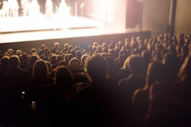 Photograph of an audience, sat looking over on to a stage.