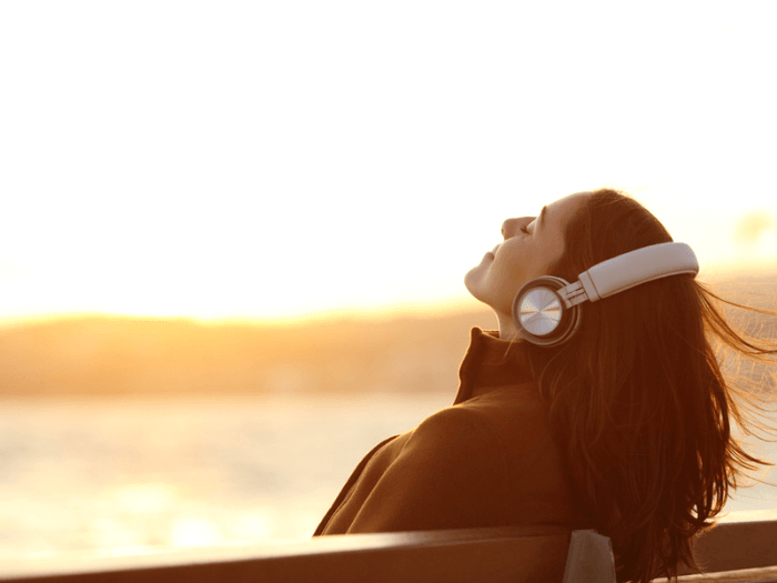 A women sat on a beach at sunset smiling while listening to headphones.