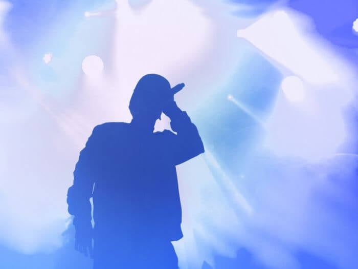 Silhouette of a rap artist performing on stage against a bright blue lights.