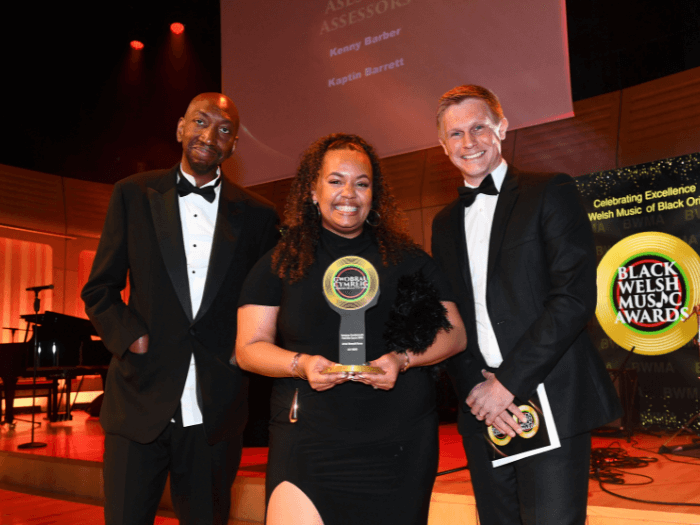 Dike Okoh, Lily Beau who is holding the award, and Andy Warnock, on stage.