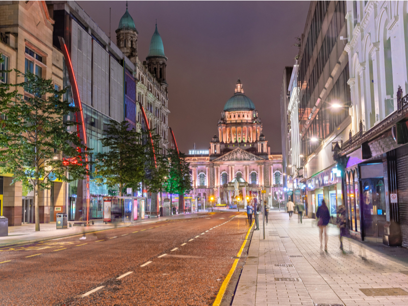 Belfast City Hall illuminated at night and seen from down a busy street with blurred pedestrians