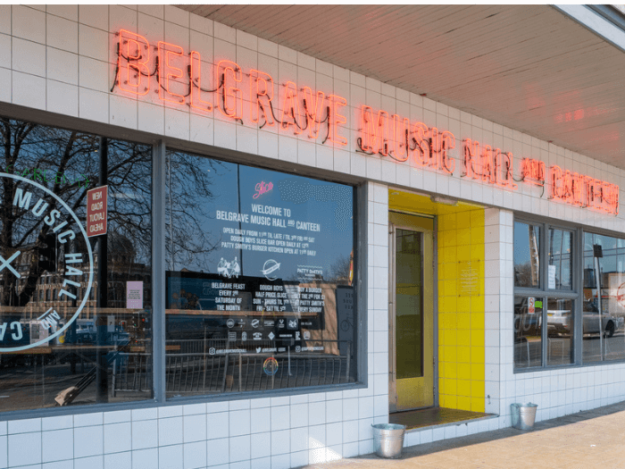 Exterior of the venue - a white tiled building with writing on the windows and an orange neon sign saying Belgrave Music Hall.