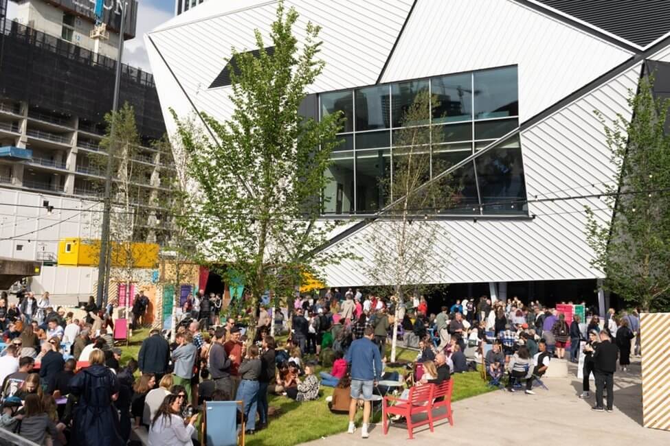 People gathered outside on the grass area of Aviva Studios’ Factory International building in Manchester.