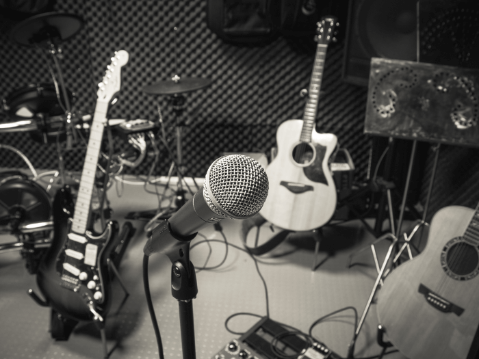 Black and white image of recording studio featuring microphone, guitars, amps, mixer and drumkit.