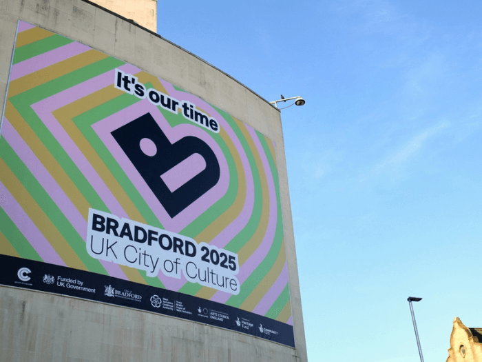 A large vibrant banner saying “It’s our time, Bradford 2025 UK City of Culture”, outside of the Science and Media Museum building.