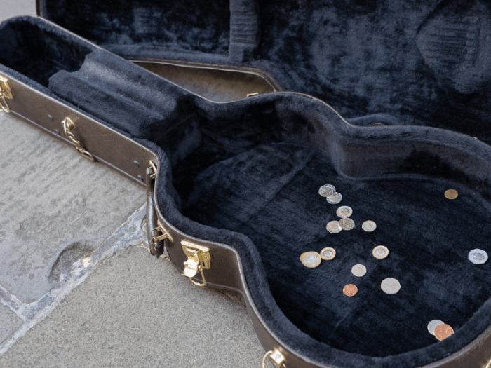 Open guitar case with some coins inside, representing busking.
