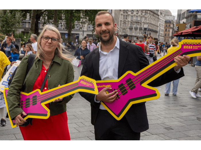 Zack Polanski with Naomi Pohl, both holding cut out purple guitars that say “The Musicians’ Union” with logo.