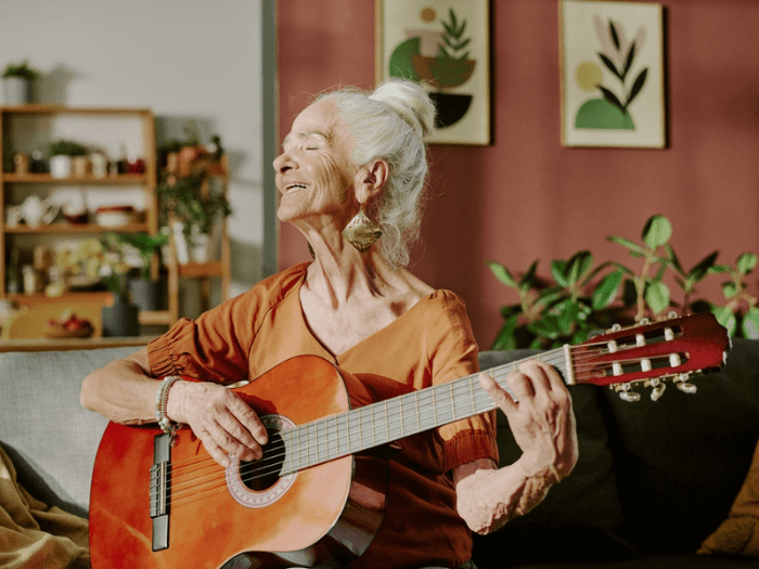 An elderly woman smiling and playing the acoustic guitar.