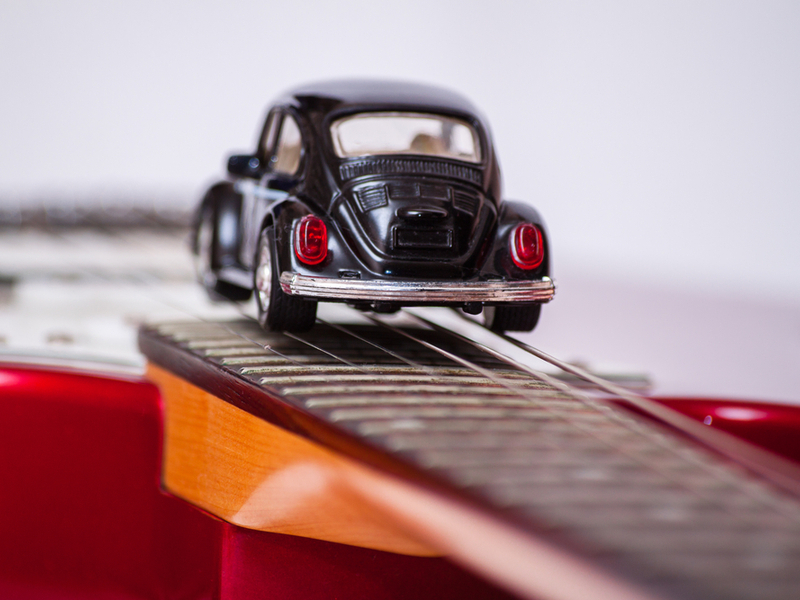 Photograph of a small model car balancing on the fret board of a guitar.
