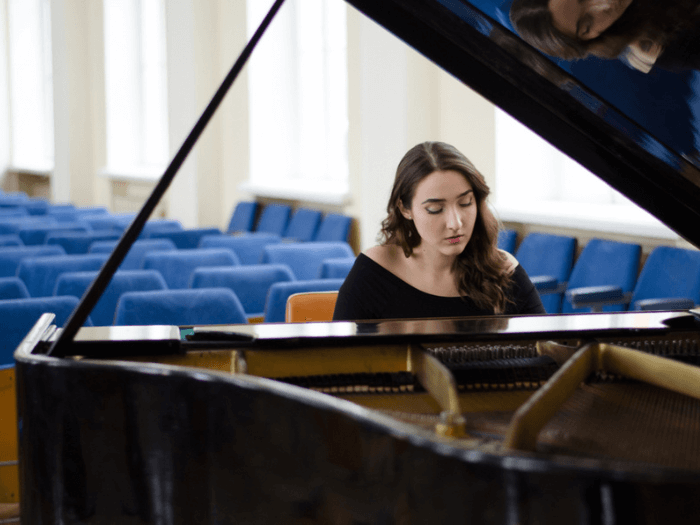 Young women sat at a piano in an auditorium.