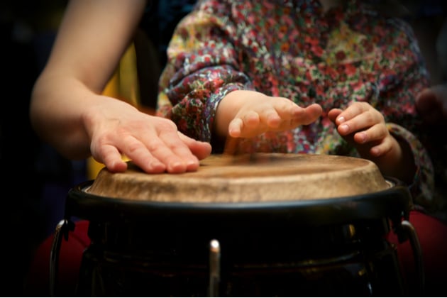 Photograph of an adult and child practising on a percussive instrument. The image shows only their hands and the skin of the drum.