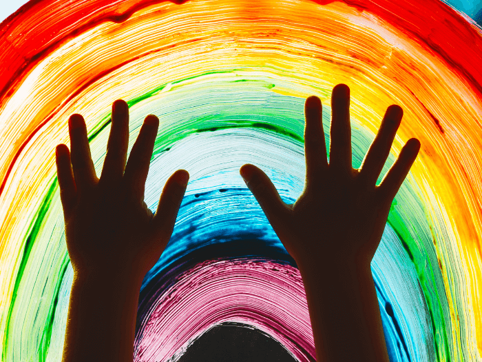 Close-up of child's hands touching a painting of a rainbow on the window.