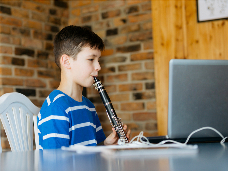 A child around 10 years old sits at a computer screen, playing on a clarinet