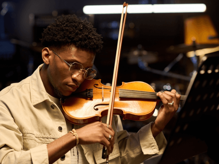A young Black musician playing the violin.
