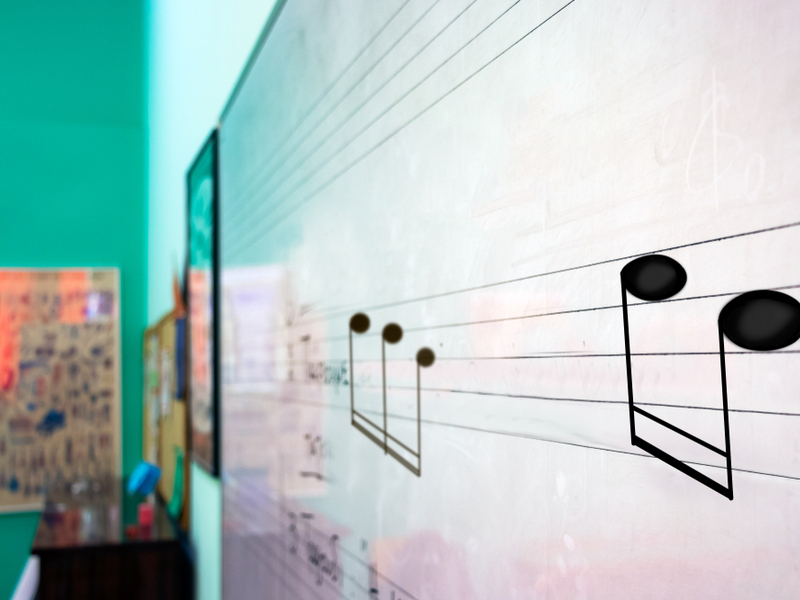 Photograph of a white board with music notation written on it, in a classroom setting.