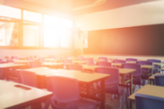 Photograph of an empty school classroom, the sun is rising through the windows with a red and orange glow