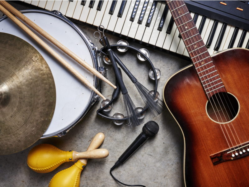 Photograph of a collection of instruments, a microphone, acoustic guitar, keyboard and various percussion.