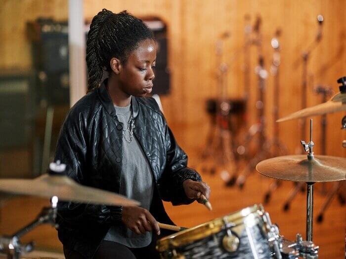 Young Black female musician playing drums in a recording studio.