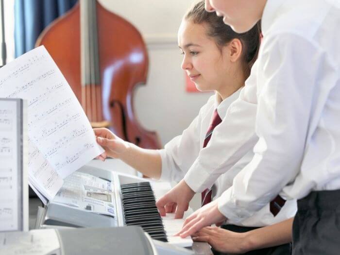 Two secondary school students in uniform reading music and playing a keyboard in class.