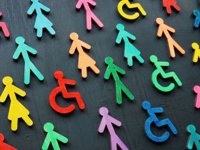 Colourful wooden symbols of people and figures in wheelchairs against a dark background, representing equality, diversity and inclusion.