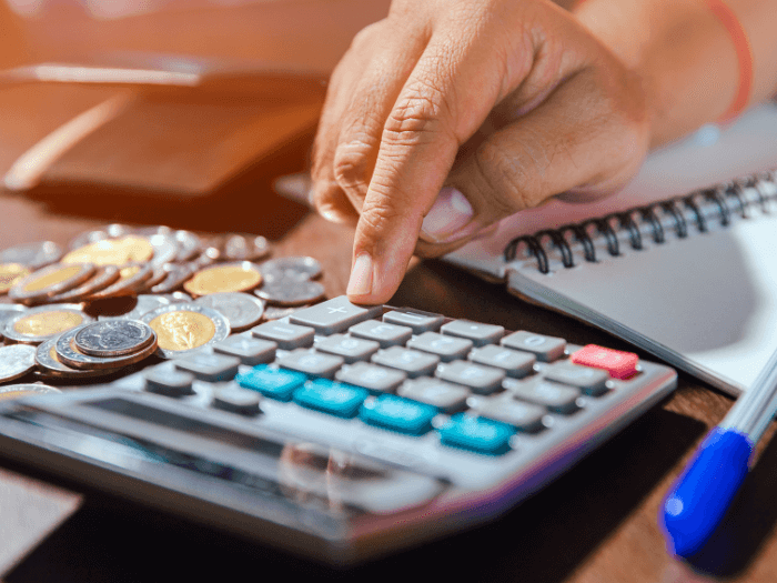 Man using calculator to count money savings and living costs. Calculator with coins and notebook on wooden table.