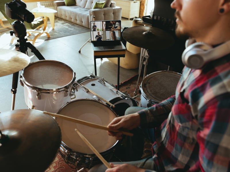 A drummer is playing on a kit in their home, a laptop computer set up near them is recording the performance.