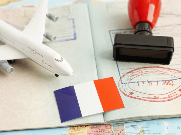 A model airplane, a small French flag and a passport and stamp all lying on a copy of the world map.