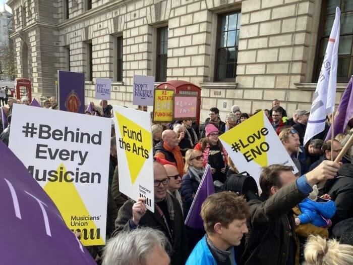 A crowd of people holding MU branded signs saying 'Fund the Arts', 'Save the ENO' and '#BehindEveryMusician' from a rally in 2022.