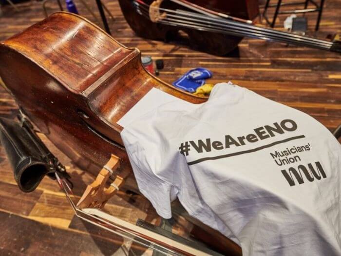 Double bass on it's side with a white t-shirt draped over it saying #weareeno with the MU logo underneath.