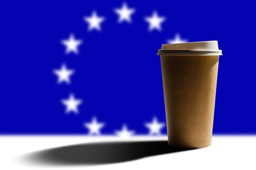 A takeaway coffee cup in front of an EU flag.