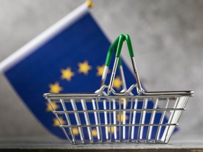 Metal shopping basket in front of an out of focus EU flag.