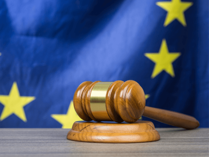 A wooden gavel on a desk in front of the European Union flag. Image credit: Shutterstock.