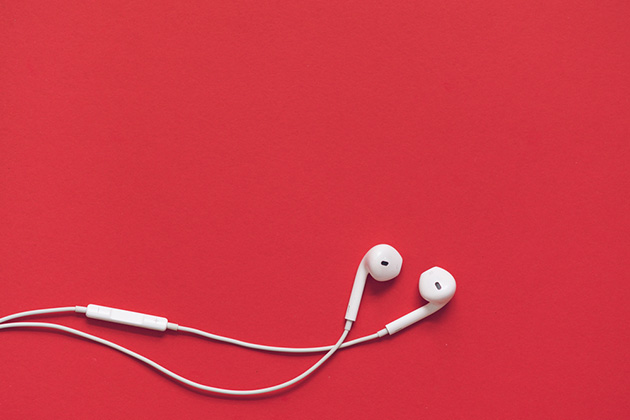 Photograph of white, iPhone style earphones with a bright red background behind them.