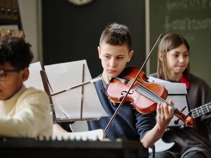 Young boy playing violin, reading sheet music, in a music classroom at school.