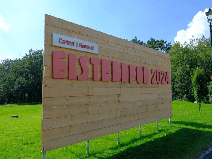 Large wooden sign saying ‘home of Eisteddfod 2024’ on a field in Pontypridd.