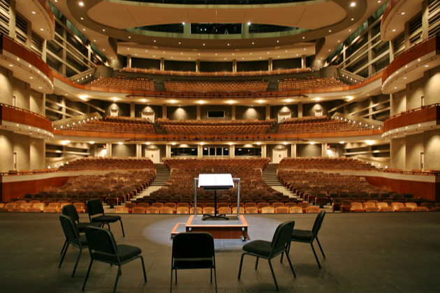 Photograph showing three chairs and a music stand in front of an empty concert hall.
