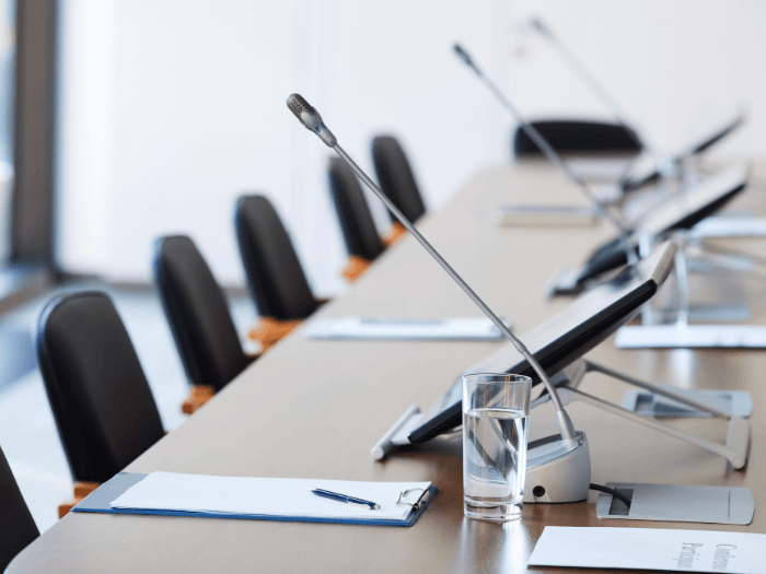 An empty conference table with chairs and microphones.