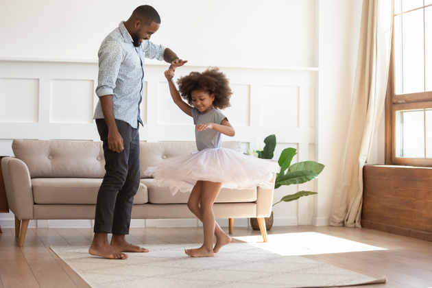 Photograph of a Black father and his young daughter dancing and joyful in the livingroom