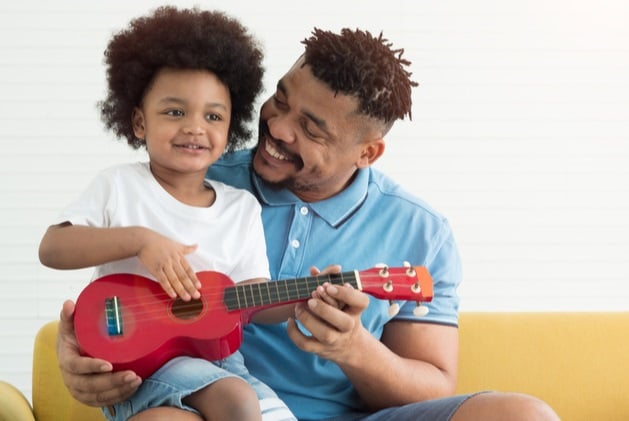 Photograph of a father and son sat close to one another, playing with a ukulele